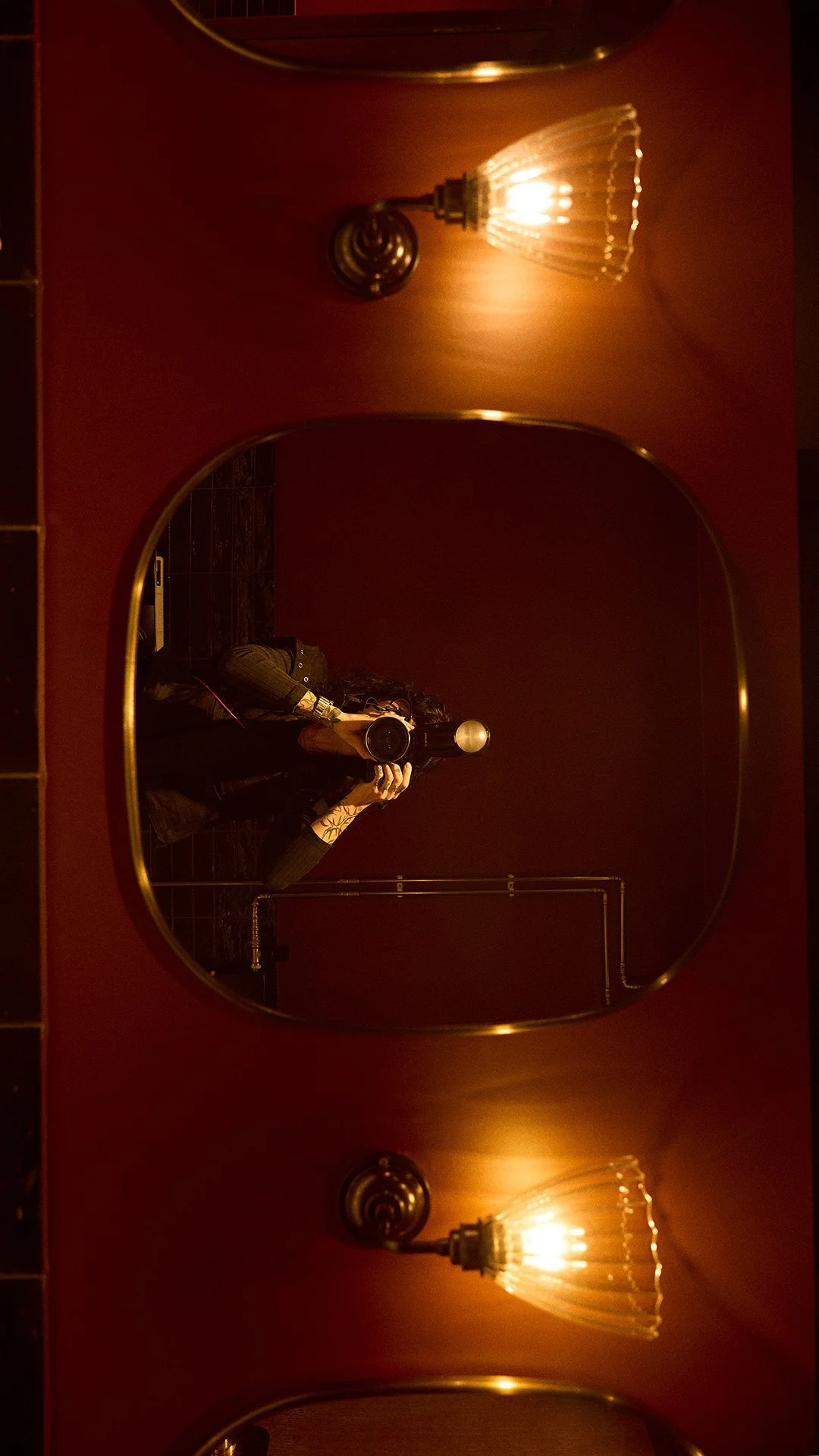 Photographer photographing herself in a mirror inside a modern bathroom, illuminated by atmospheric moody light.