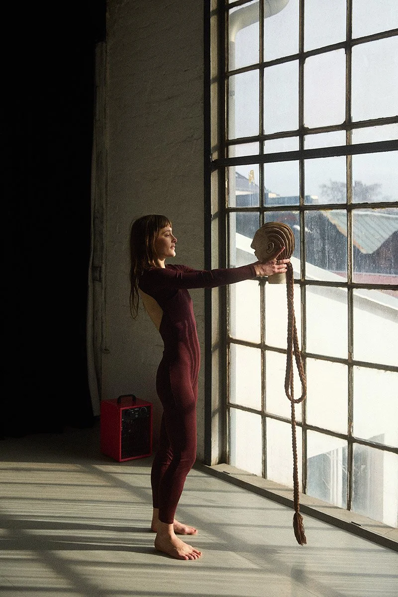 Young female artist Linde van der Burgh holding a sculptural head and gazing at it against a window at Kaos Berlin