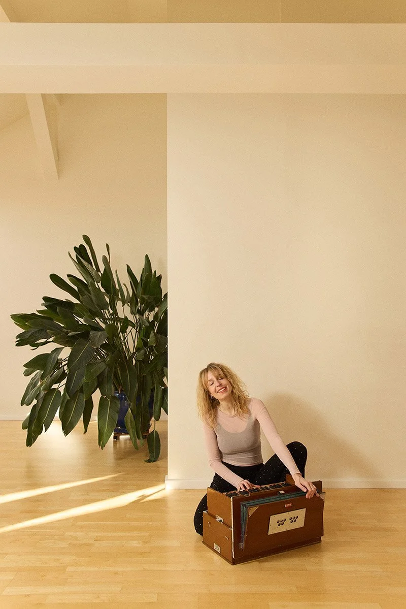 Young curly blond yoga teacher is chanting and playing on harmonium in a sun lit yoga studio in Berlin photographed by Tereza Konarikova