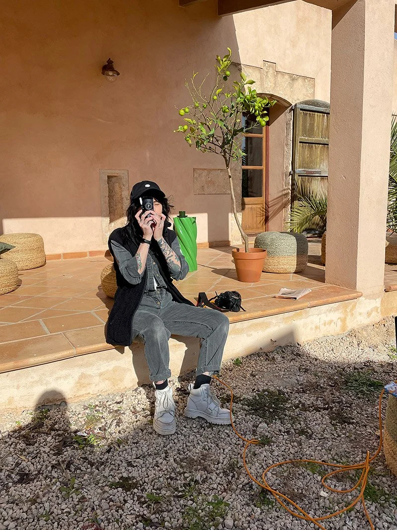 Portrait of a photographer Tereza Konarikova holding a camera in front of her face outside a Mediterranean summer house on set.