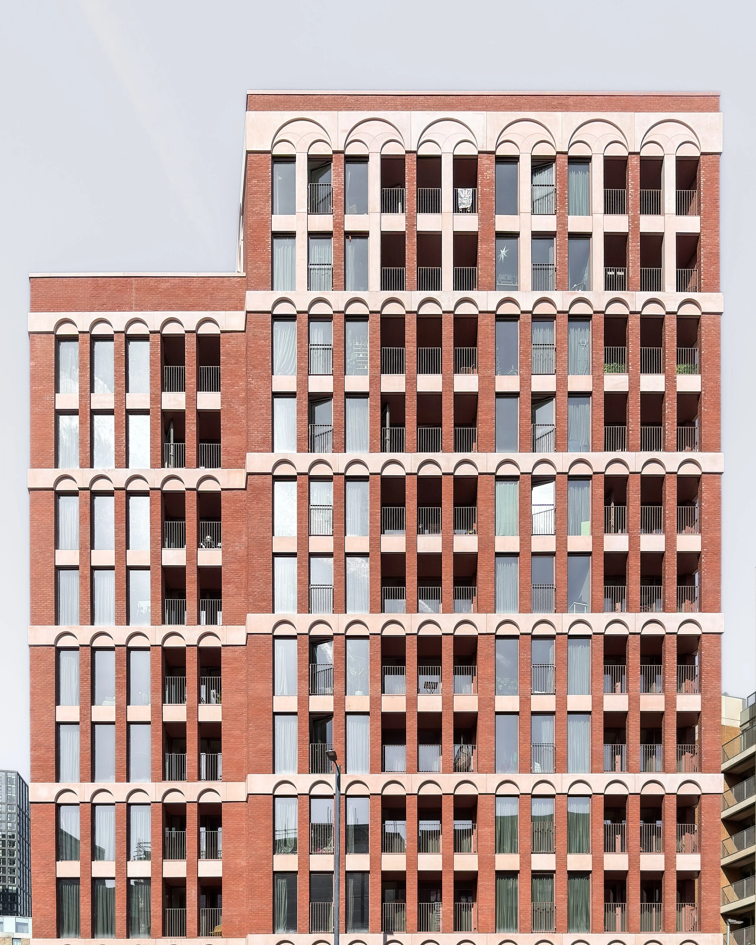 A tall brick apartment building with multiple floors and arched windows, some with curtains and balconies, under a clear sky.