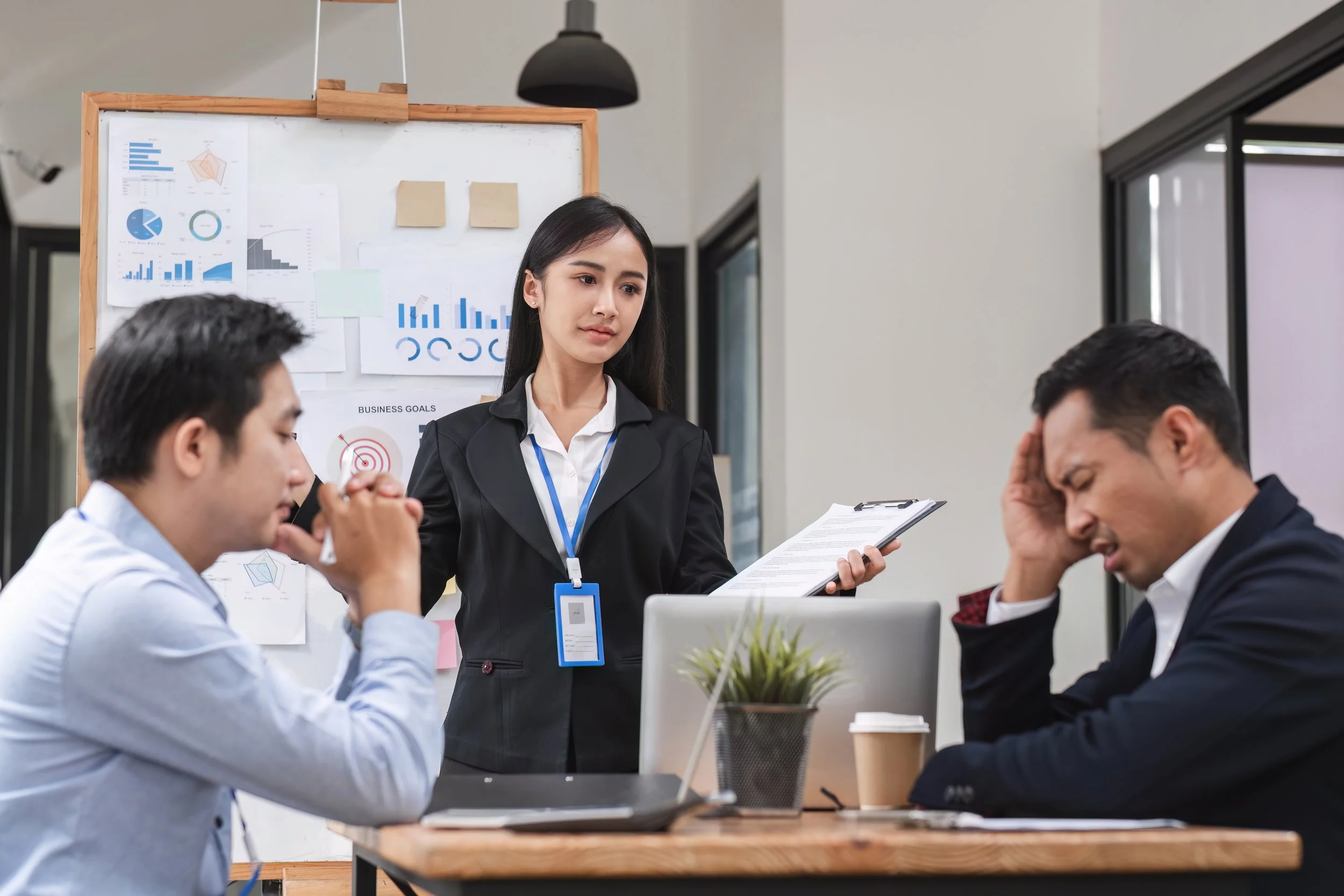Two people looking disappointed at business results. They are at a table in from of a whiteboard with charts.