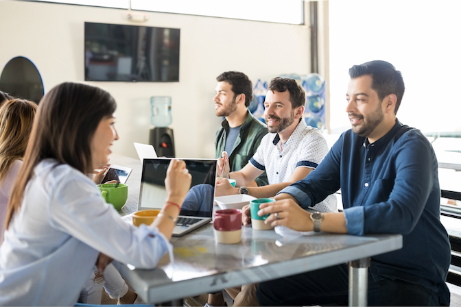 Employees sitting at a lunch table chatting with food and laptops on the table