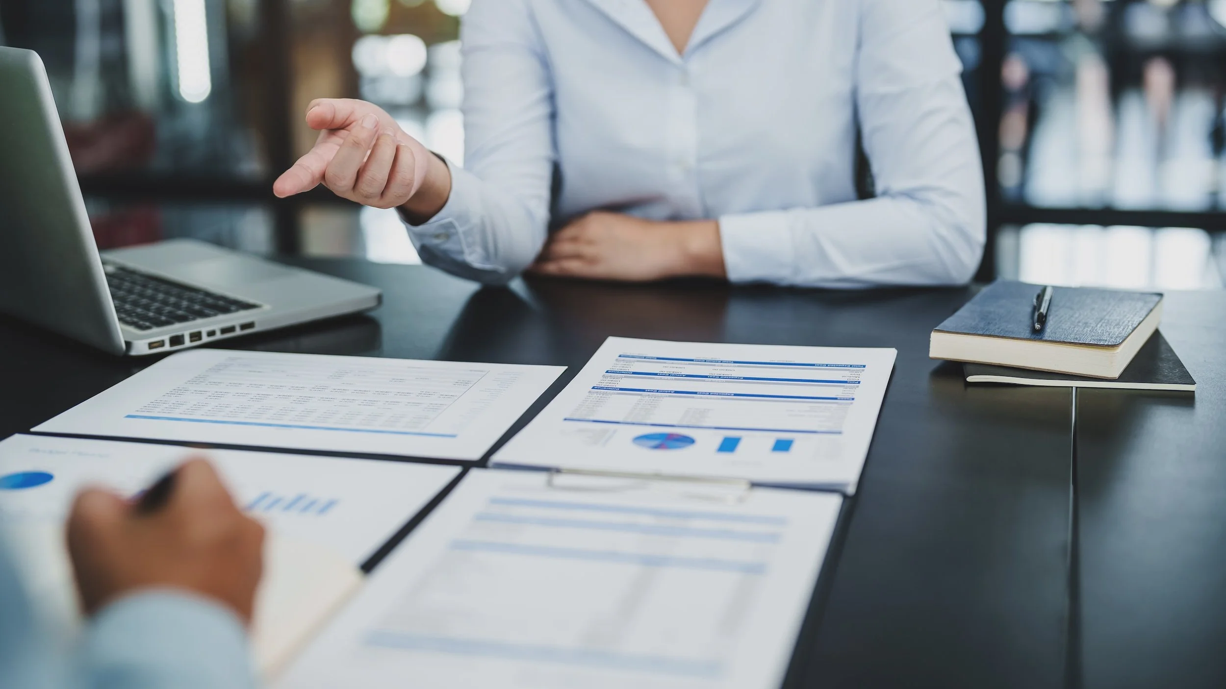 Business woman at a table pointing at charts with delegated authority from an owner of multiple businesses