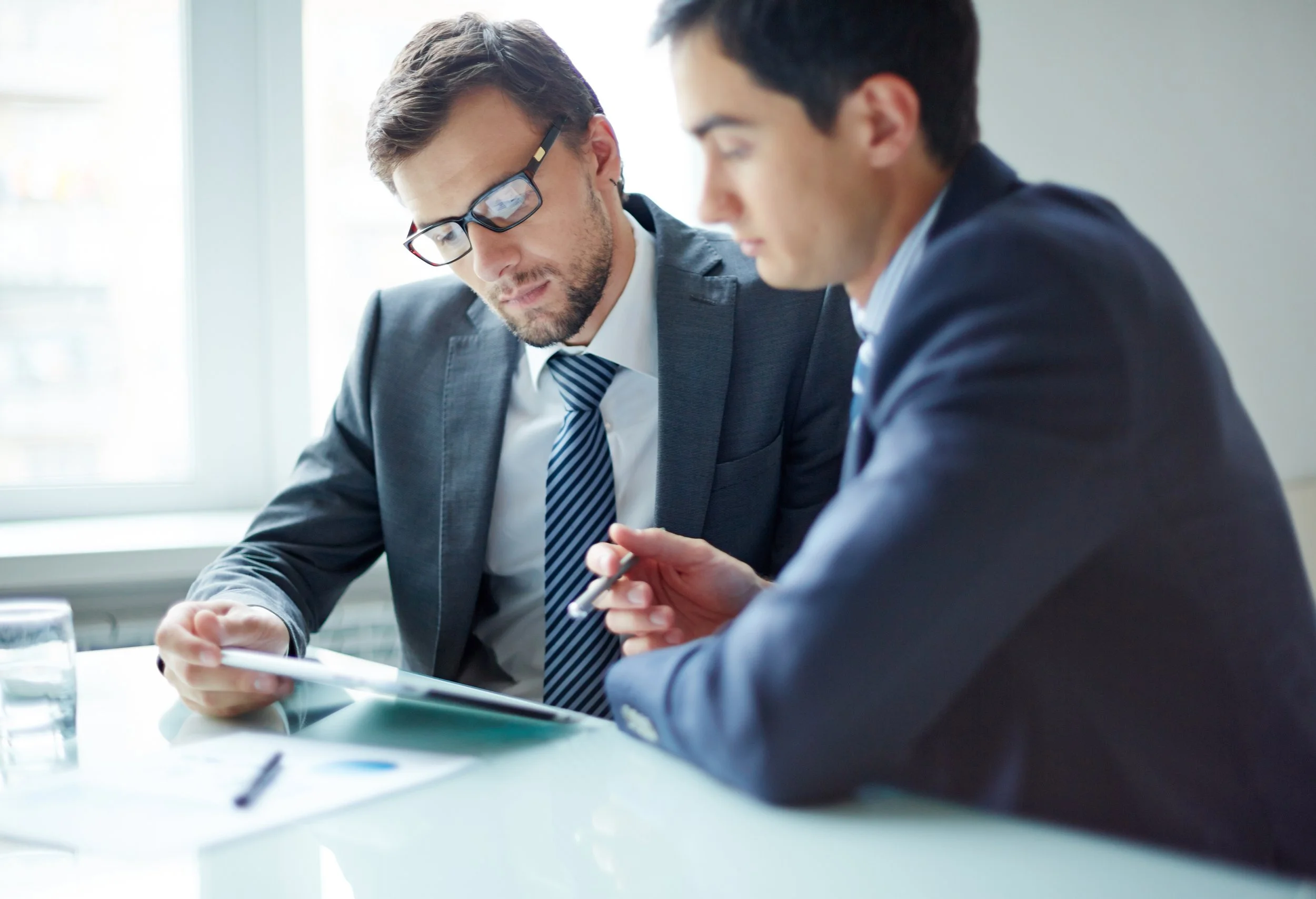 Two male business leaders in suits look over a report contemplatively while sitting at table