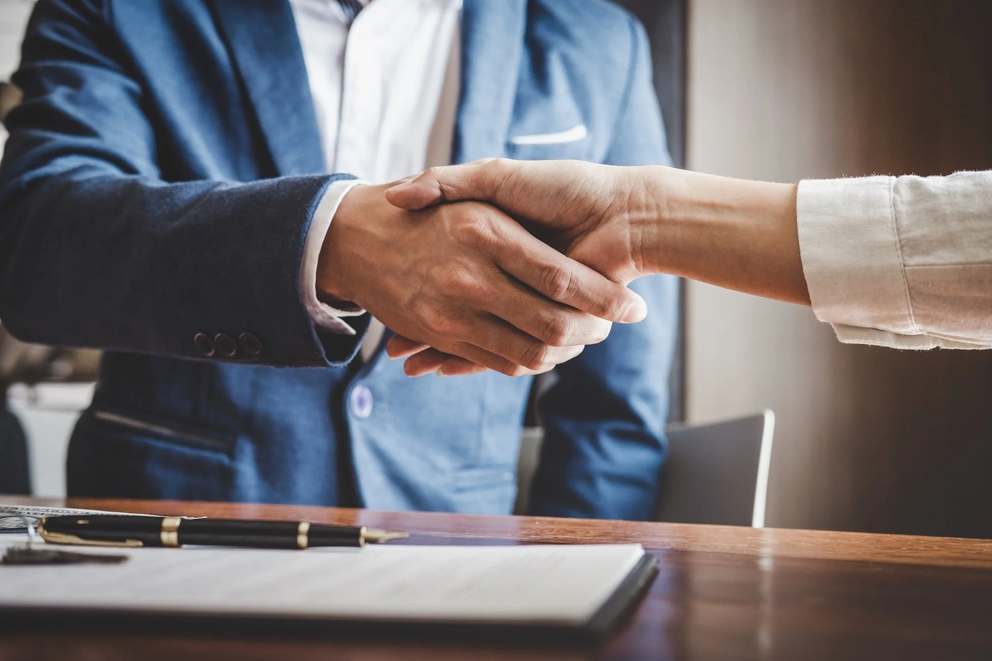 Business Man in a suit shaking hands about a Private Equity Agreement with another business woman over a table with a pen.