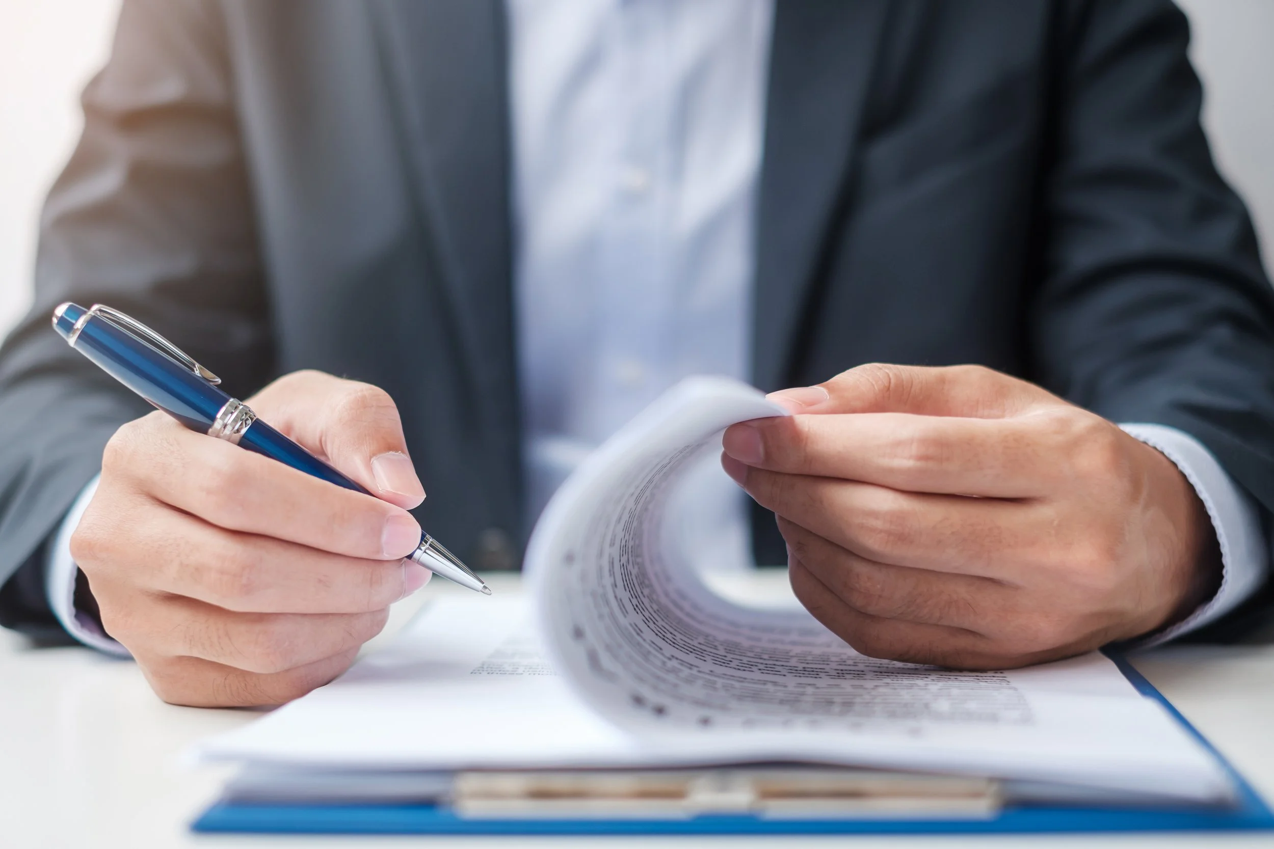 A person in a business suit holding a pen and reviewing documents.