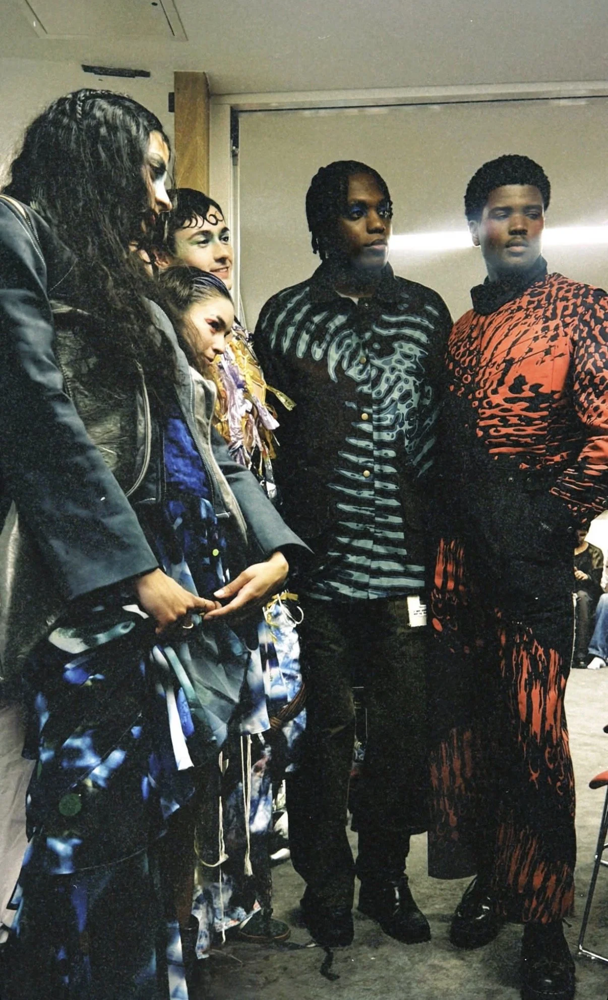 Group of five people standing together indoors, dressed in bold, colorful clothing and looking to the right.