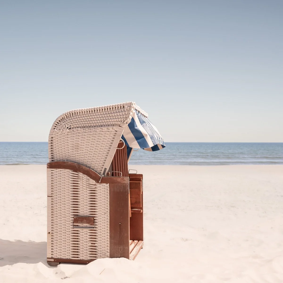 Een strand met zonwering en een zee op de achtergrond. De typische strandstoel van het Duitse eiland Rugen.