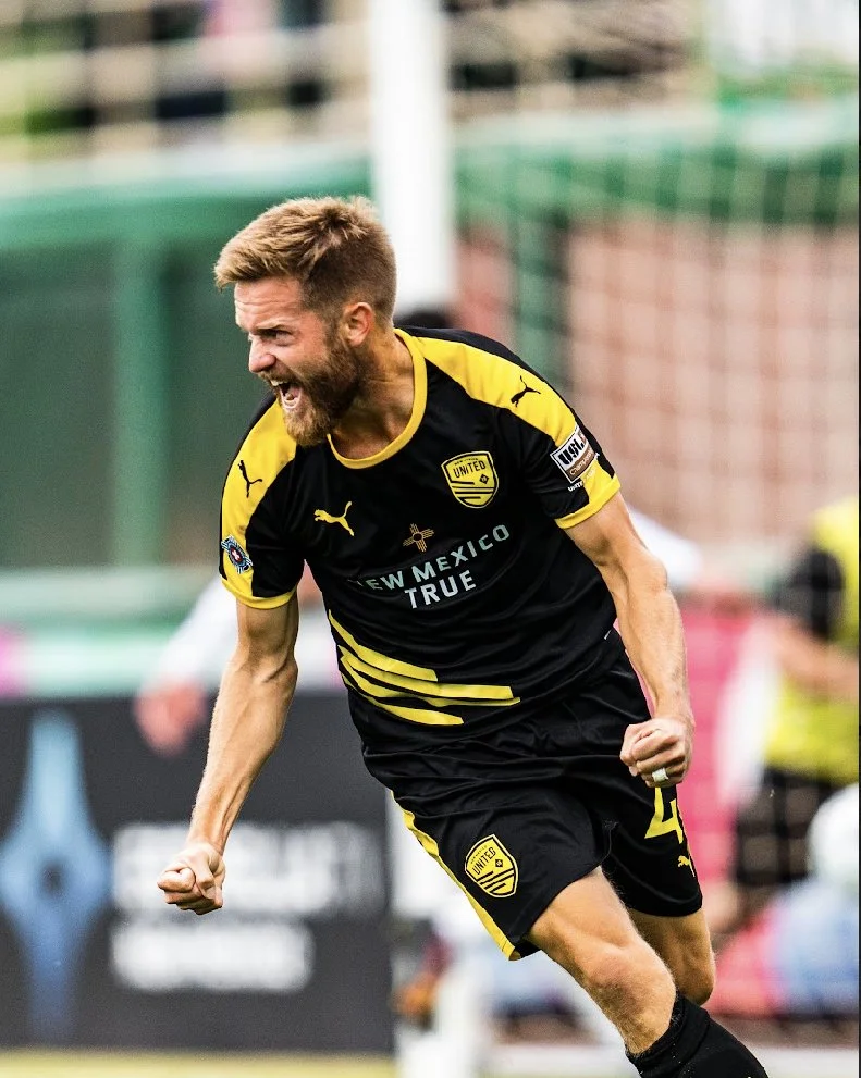 Chris Wehan is celebrating a goal he scored on the soccer field, clenching his fists and shouting with joy.