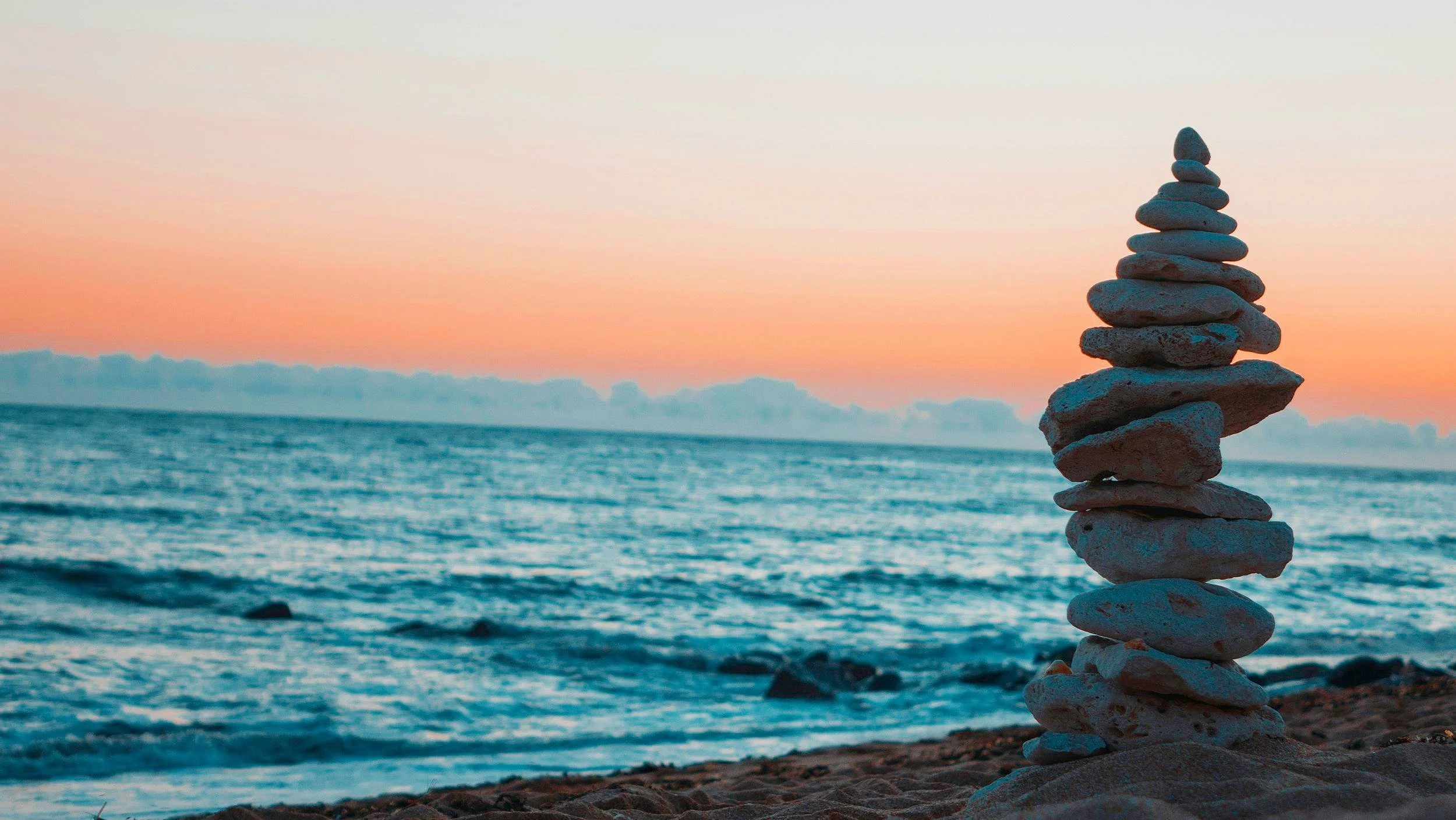 A stack of smooth stones beside rolling water under an orange evening sky.