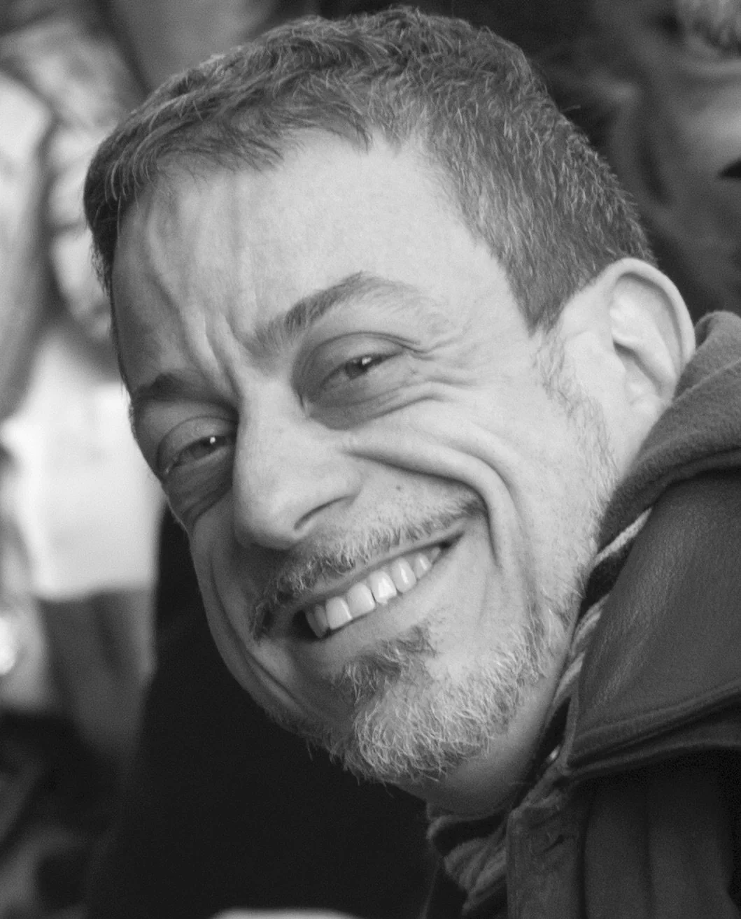 Close-up of a smiling man with short hair, a beard, and wearing a jacket, in black and white.