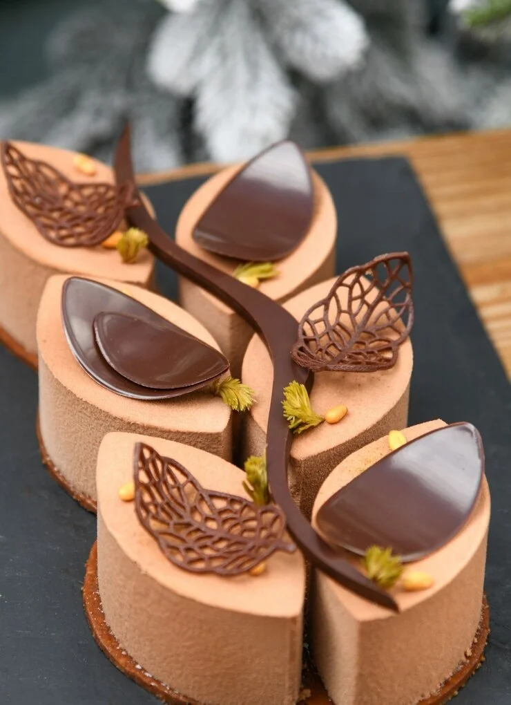 Gâteau chocolaté décoré de feuilles en chocolat et de petites fleurs en forme de petits bouquets, présenté sur une assiette noire.