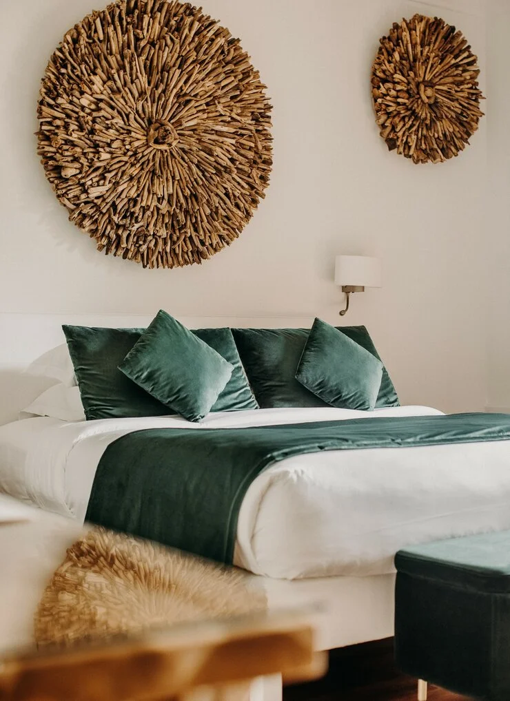 Chambre avec lit à baldaquin blanc, oreillers en velours vert foncé, décoration murale avec deux œuvres en bois de formes rondes, lampe murale blanche