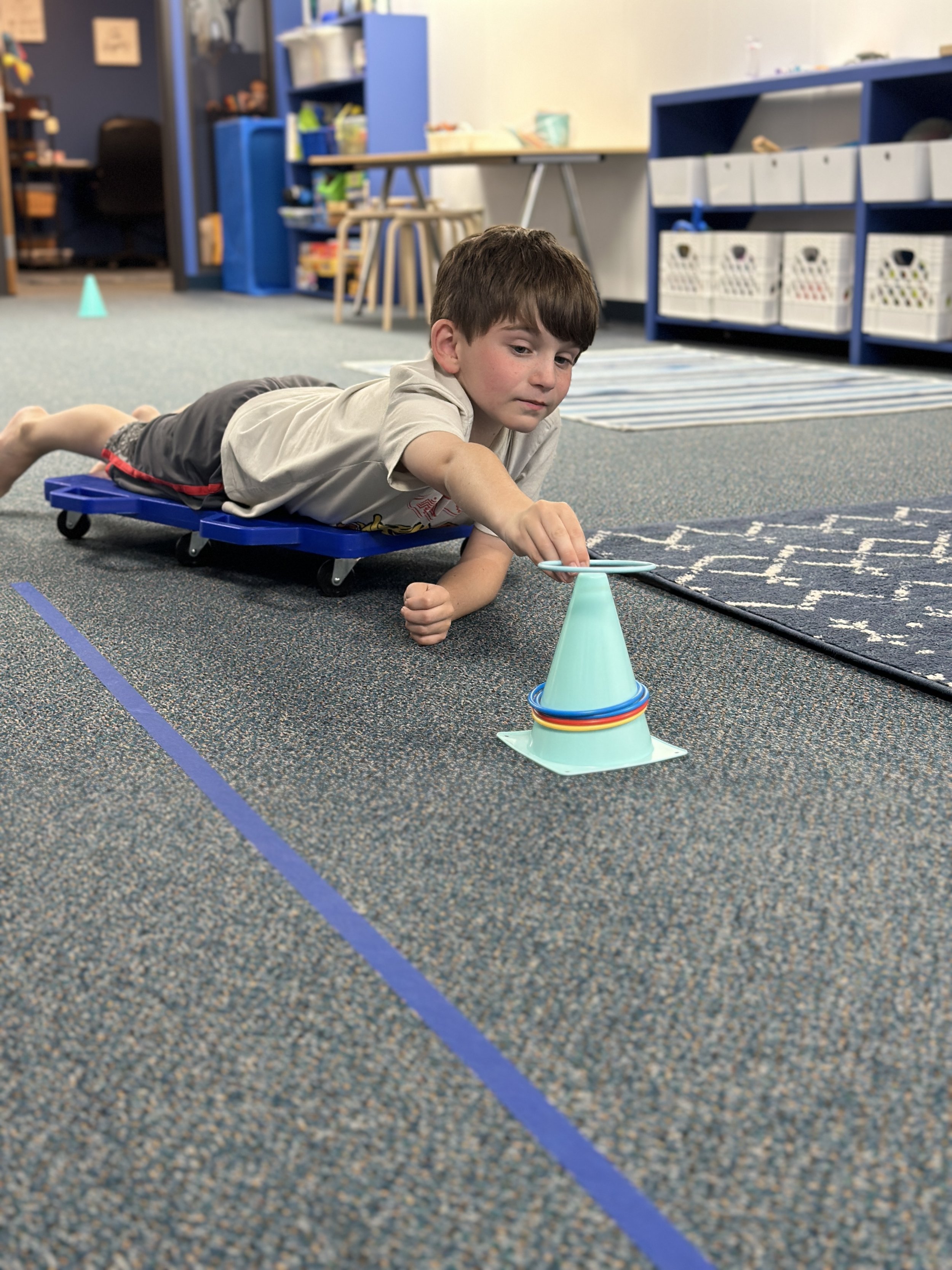 Boy playing ring toss while on a tummy scooter to support Landau Reflex integration and core strength development