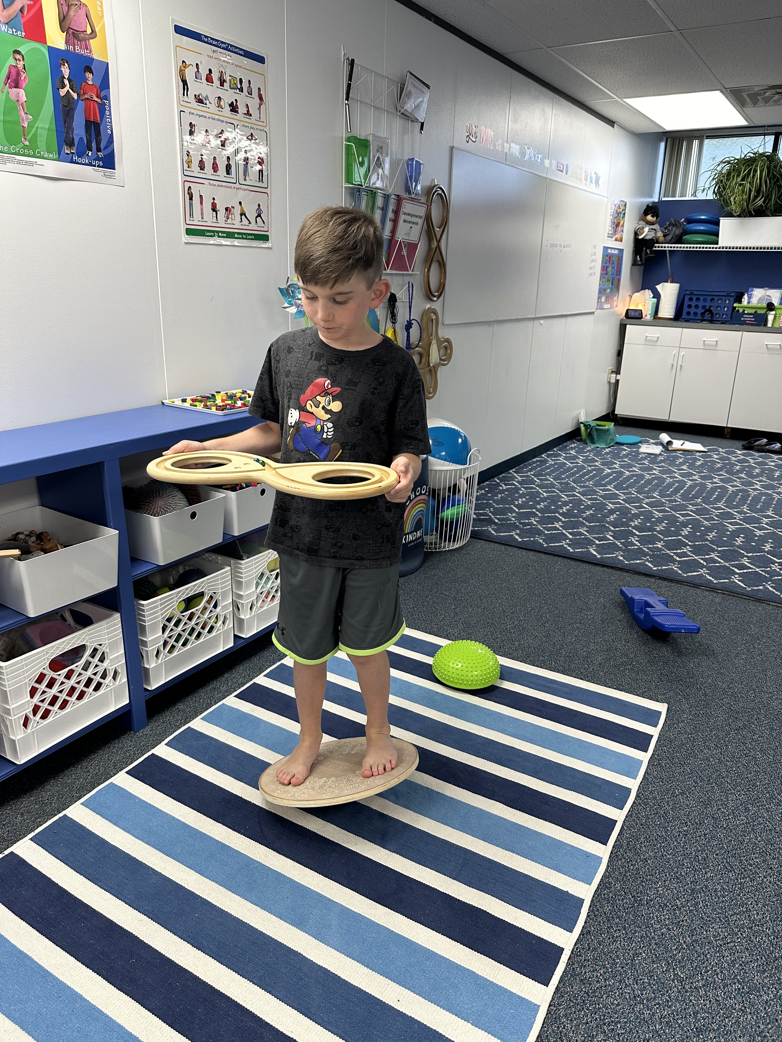 Boy balancing on balance board while using infinity loop marble board to enhance coordination and reflex integration