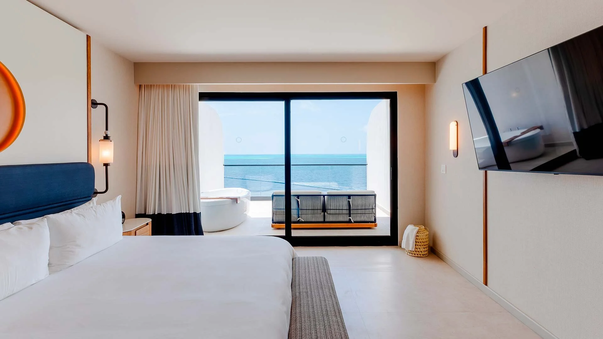 Hotel room with a large bed, sea view balcony, hot tub, and ocean view through sliding glass door.