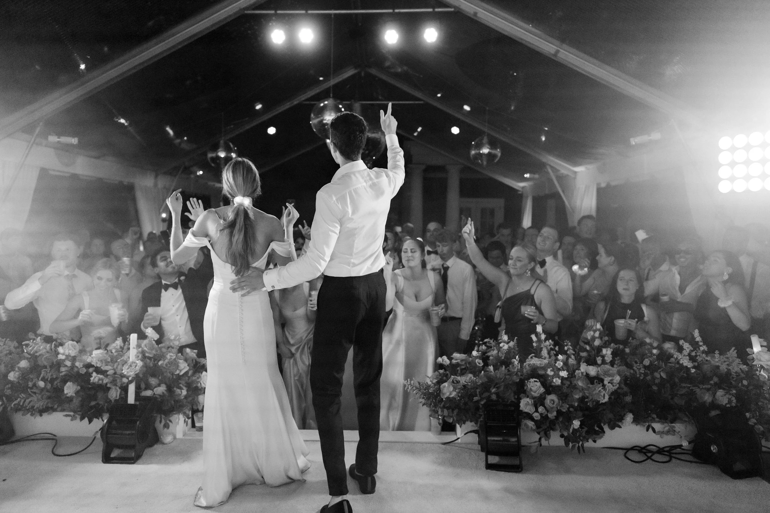 Bride and groom on stage during a black-and-white tented wedding reception with guests dancing at a Kiawah Island celebration.