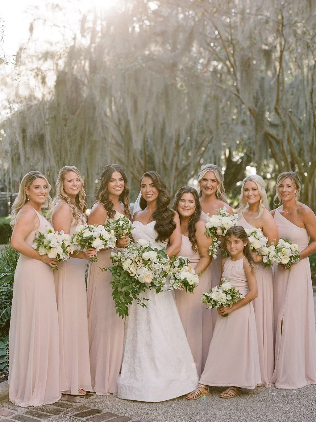 Bride with her bridesmaids and flower girl outdoors at a Kiawah Island wedding, carrying white and green floral bouquets.