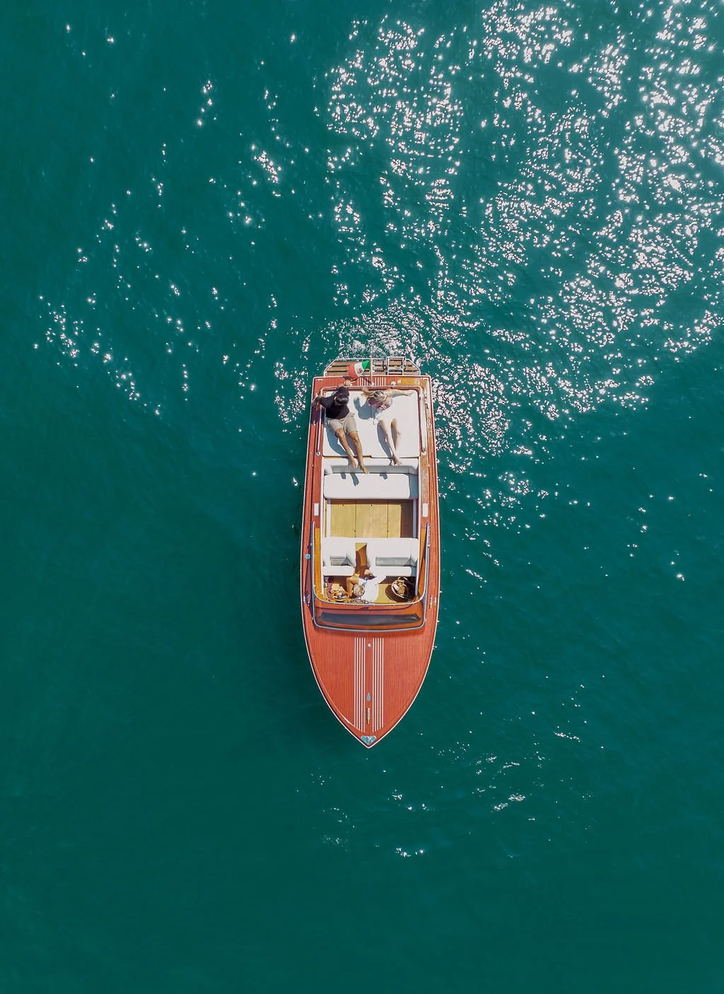 Aerial view of a wooden boat floating on bright blue water with a couple relaxing onboard during an intimate Italy elopement.