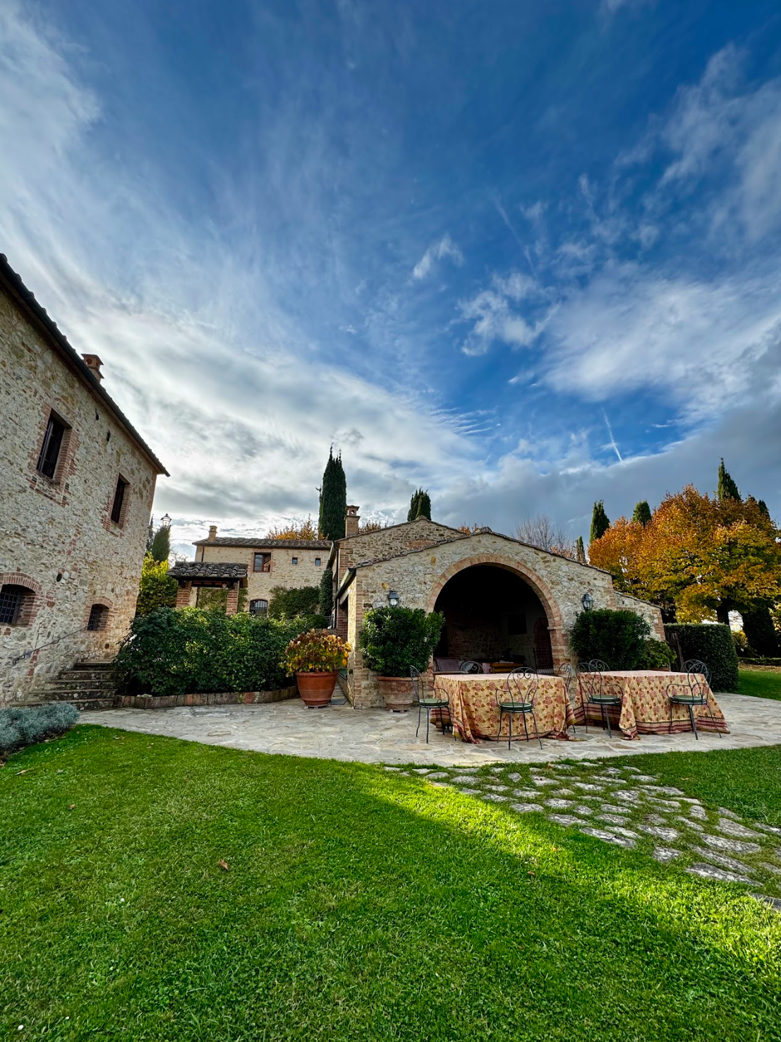 Stone villa courtyard in Tuscany with patterned linens, arched architecture, cypress trees, and blue sky for a destination wedding venue.