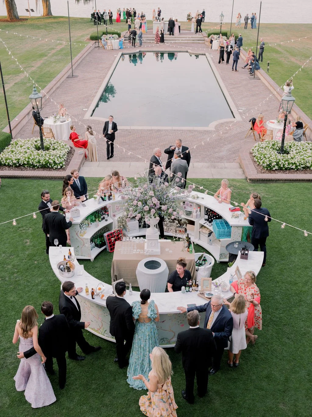 Guests gathering around a circular floral bar during a poolside cocktail hour at an East Coast estate wedding.