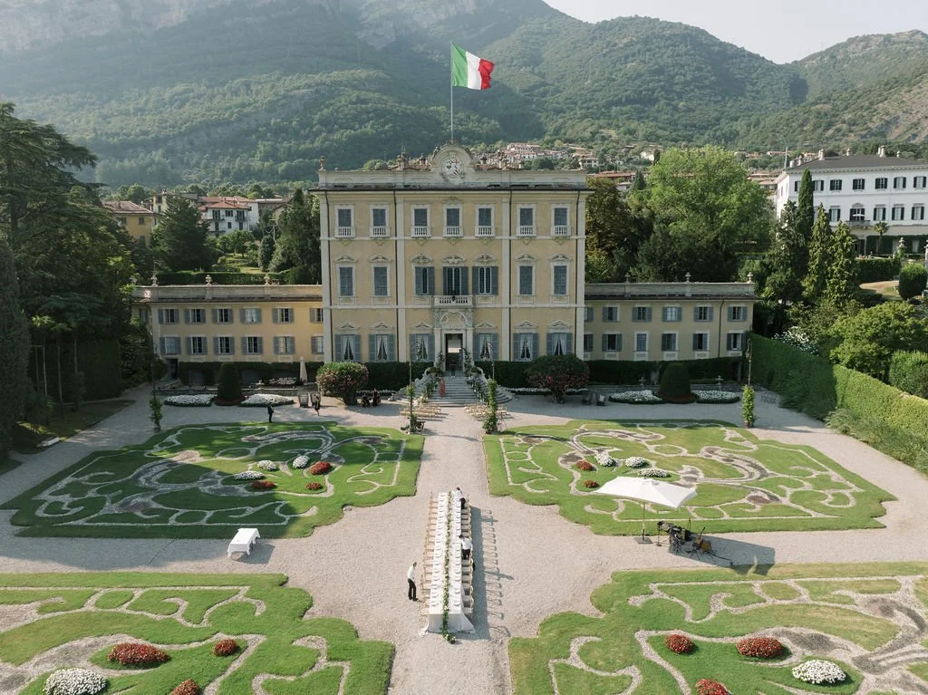 Aerial view of a Lake Como villa wedding ceremony setup with formal gardens, mountain views, and an Italian flag.