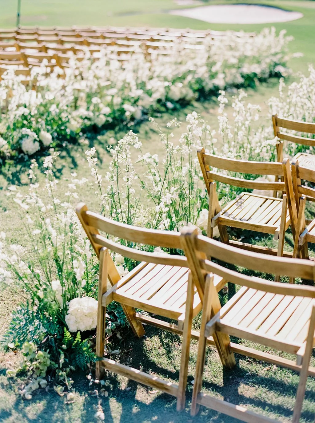 Wooden ceremony chairs beside a white flower-lined wedding aisle overlooking the River Course on Kiawah Island.