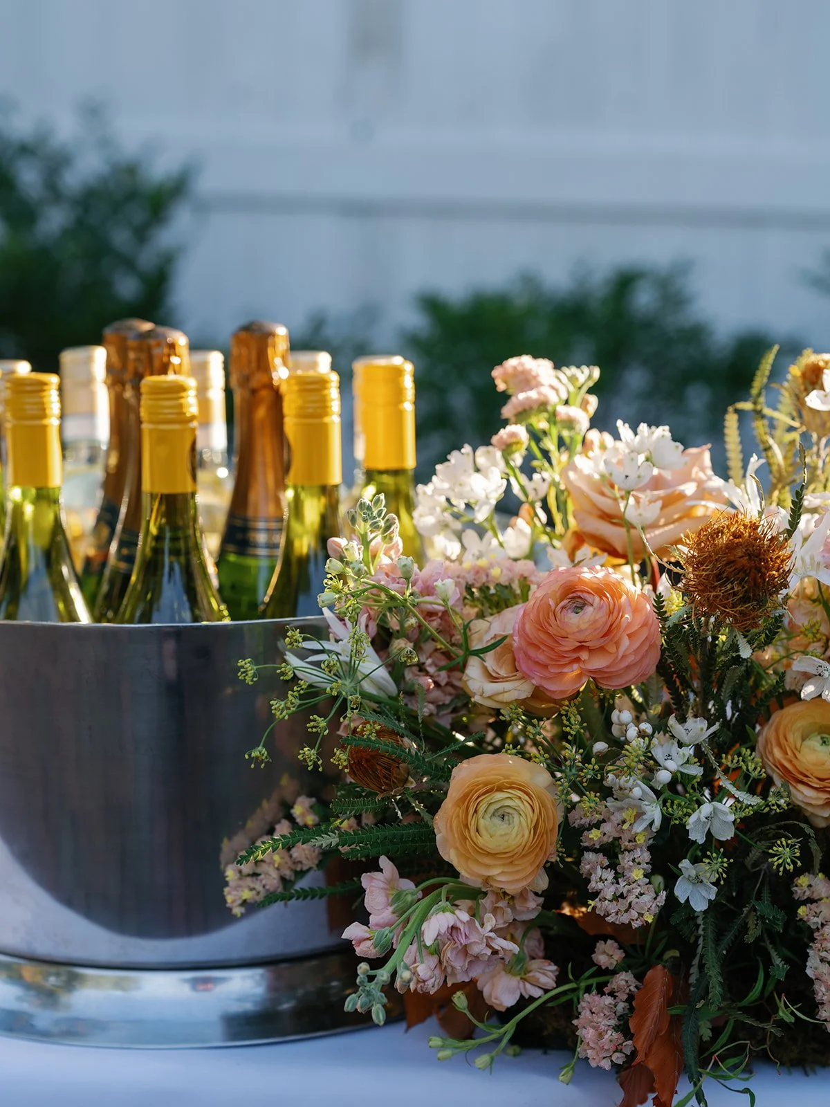 Close-up of chilled wine bottles beside a soft peach and blush floral arrangement on a welcome party bar.