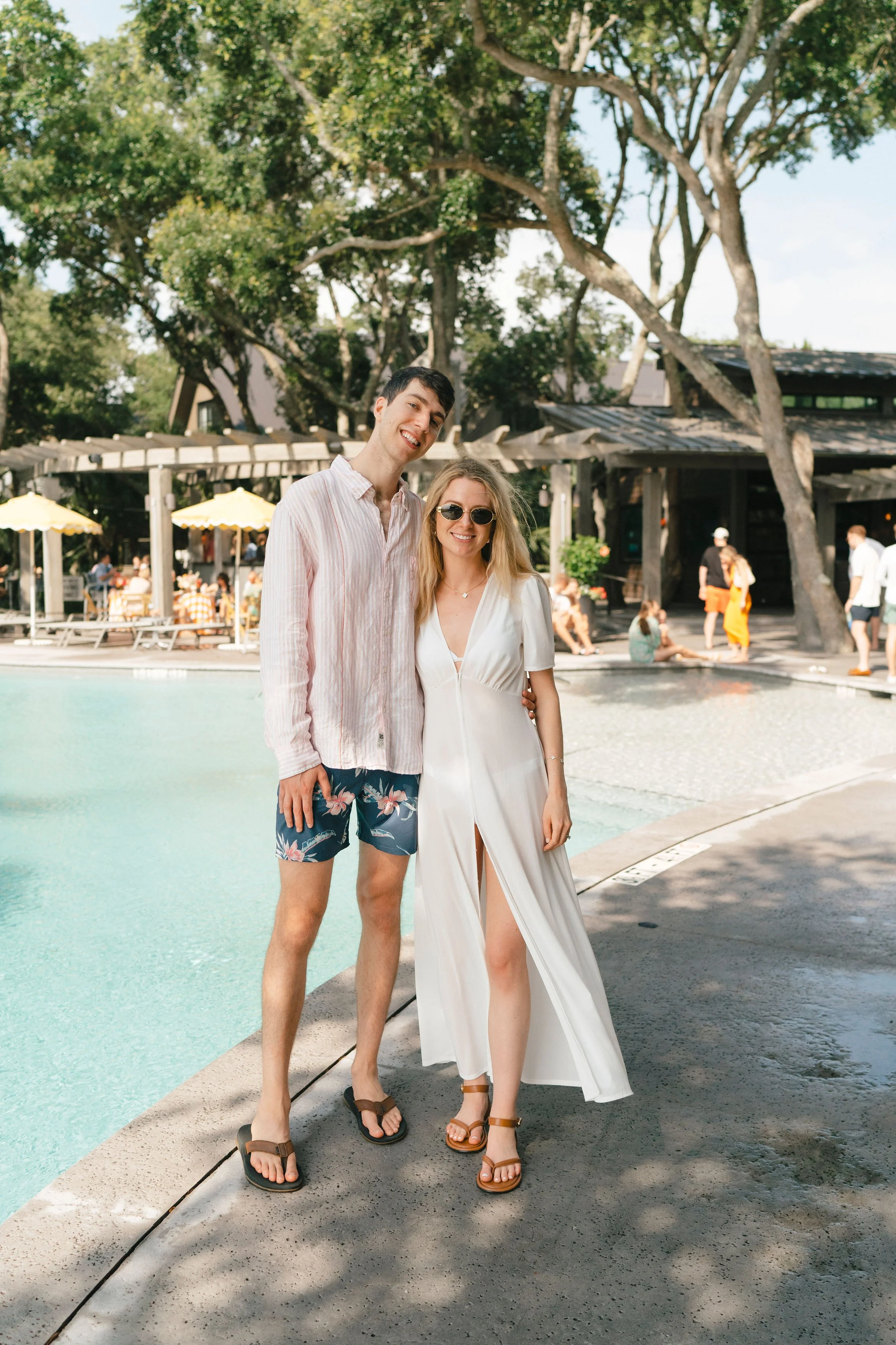 Couple in resort attire posing by the pool during a casual destination wedding farewell brunch.