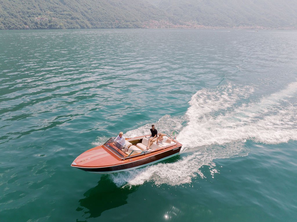 A couple riding across Lake Como in a classic wooden boat, a quintessential experience during an Italy destination wedding weekend.
