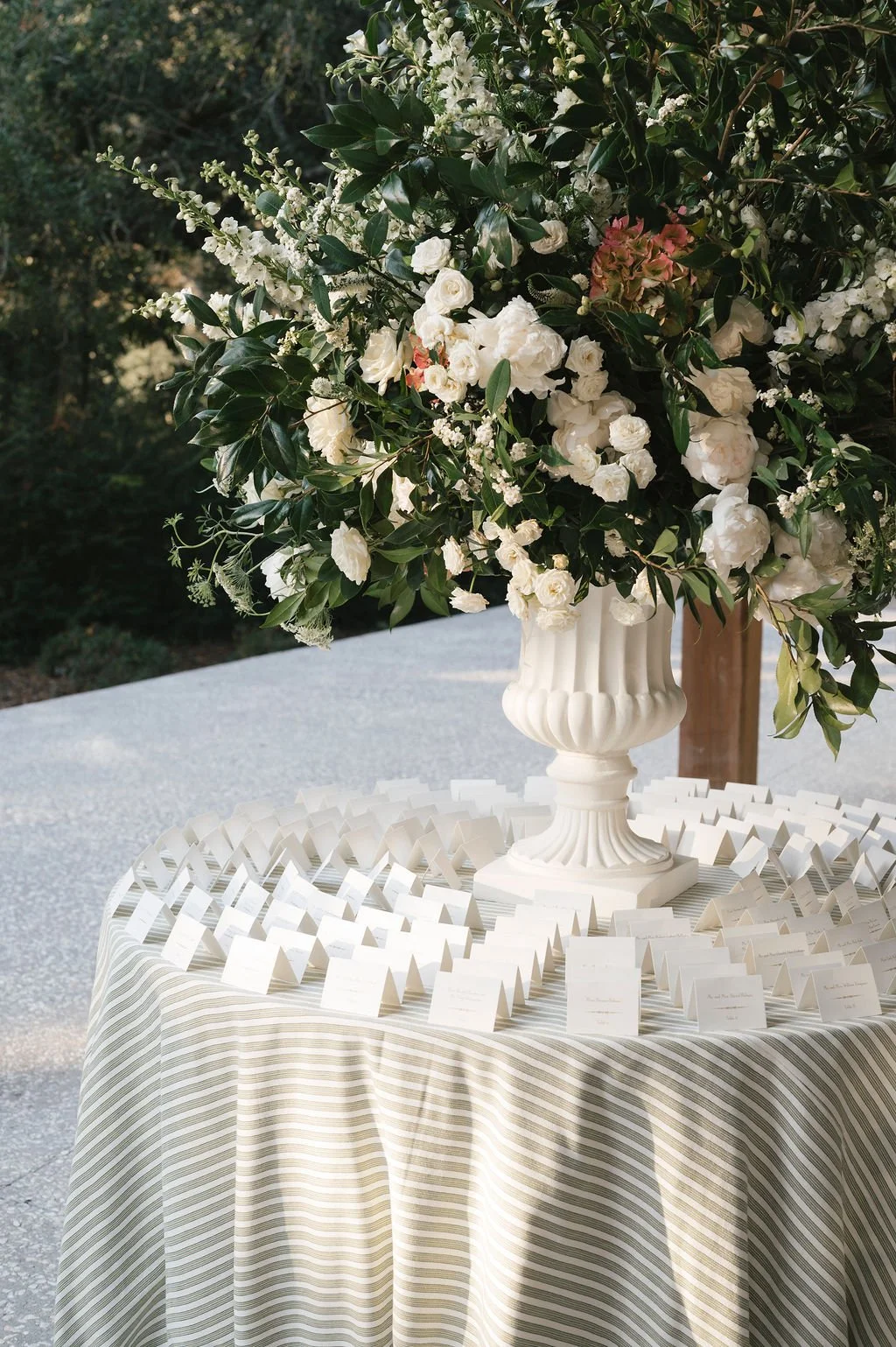 Wedding escort card table with striped linen, white urn floral arrangement, and neatly arranged place cards.
