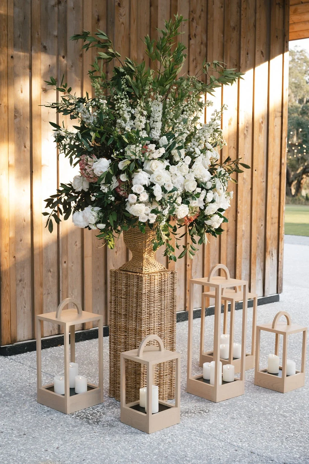 Oversized white floral arrangement in a wicker urn with wooden lanterns for a Charleston wedding arrival moment.