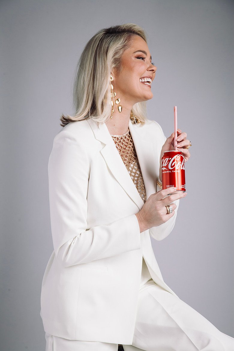 Podcast guest in a white suit holding a Coca-Cola, smiling during an editorial studio portrait for a conversation on branding, influence, and entrepreneurship.