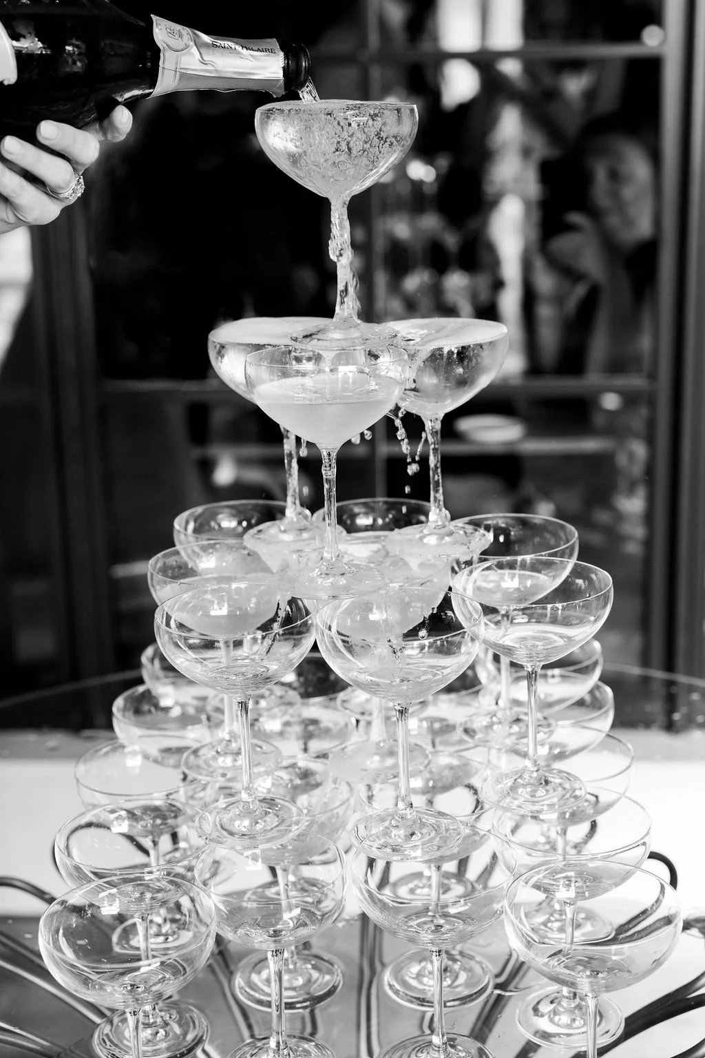 Champagne being poured into a stacked coupe glass tower during a destination wedding celebration.