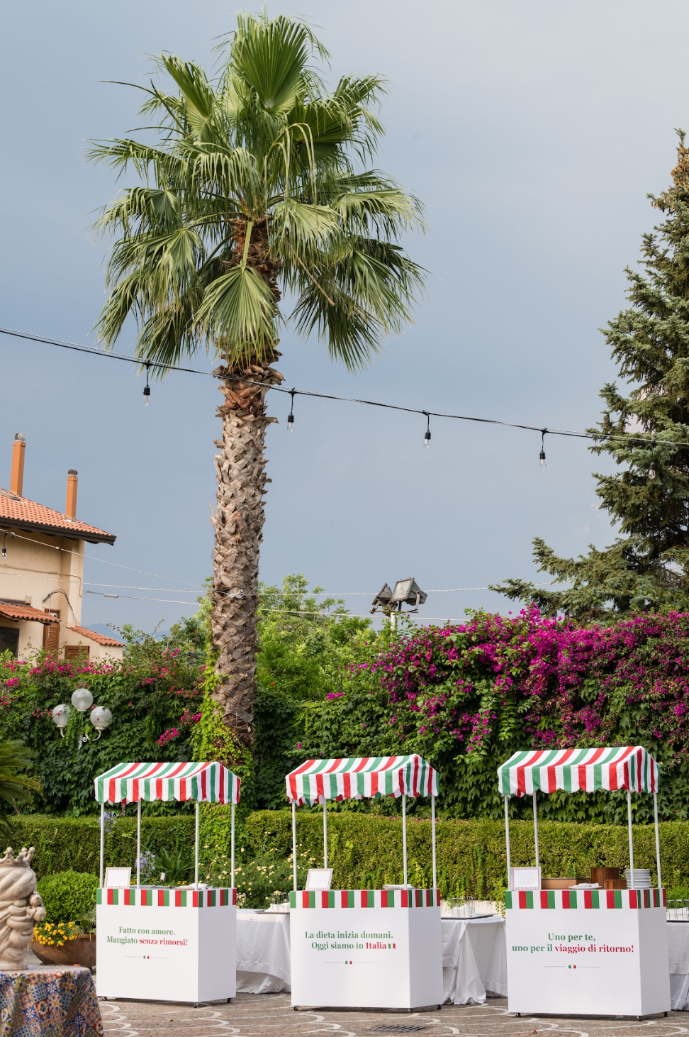 Red, white, and green striped food stations set among palm trees and bougainvillea for an Italy wedding celebration.