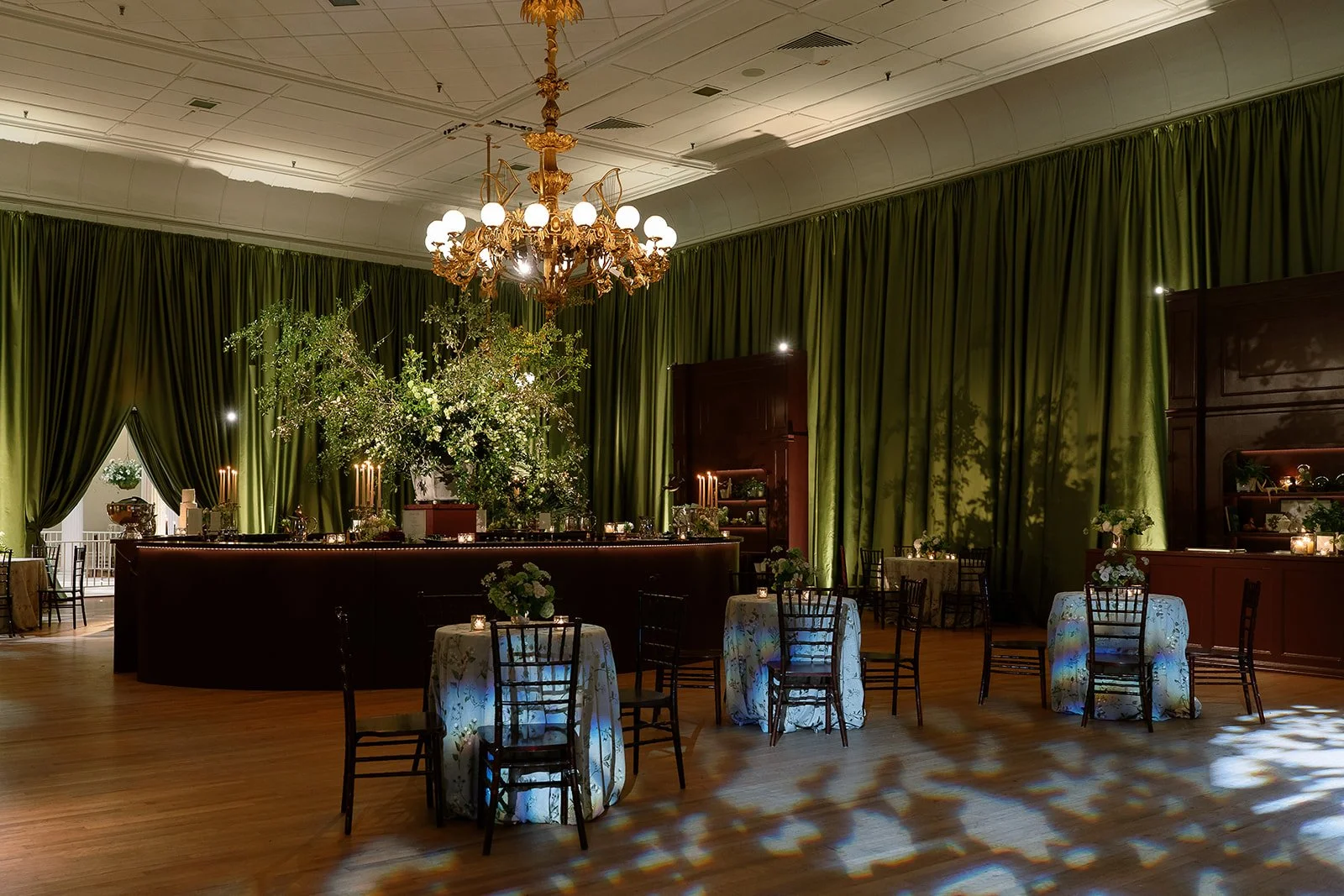 Charleston wedding reception inside Hibernian Hall with olive green draping, a central bar, organic greenery, candlelight, and cocktail tables.