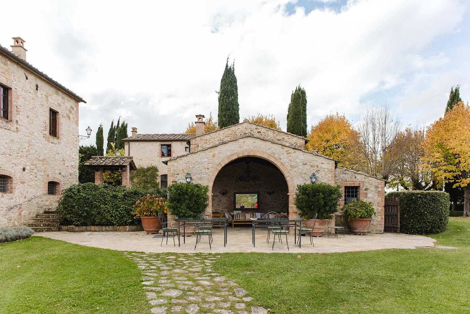 Stone courtyard at a Tuscan villa with an arched loggia, terracotta pots, garden seating, and historic farmhouse architecture.
