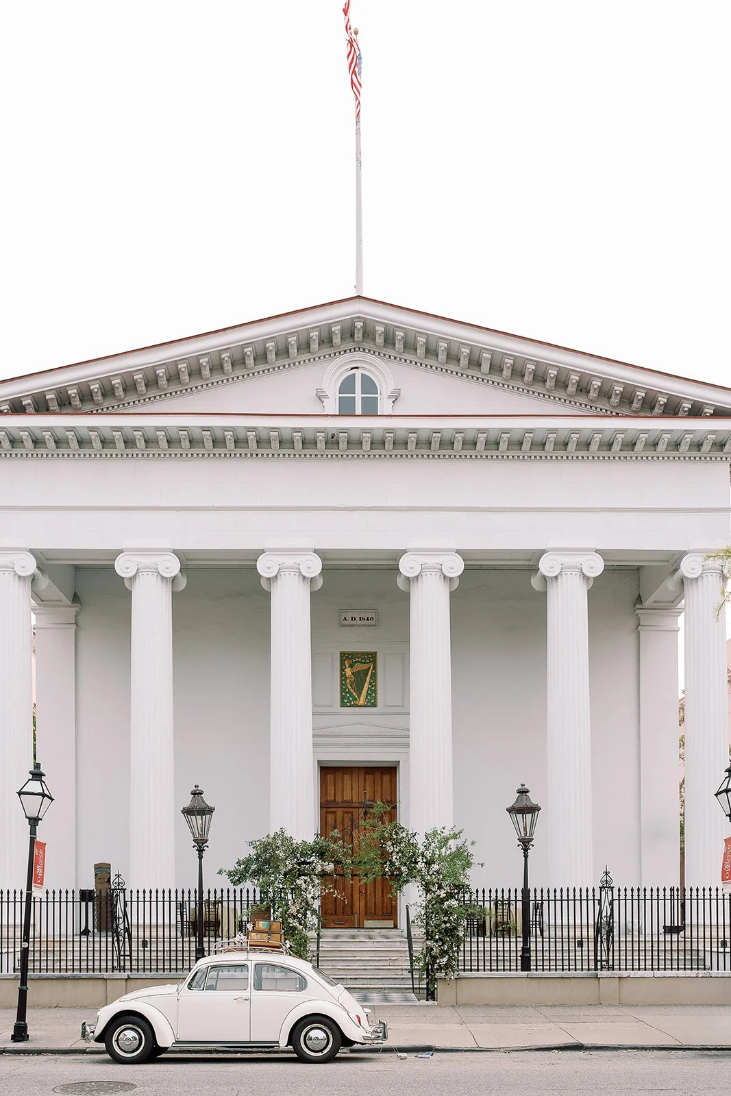 Historic Charleston church with white columns, floral entry detail, and a vintage white getaway car for a sophisticated wedding weekend.