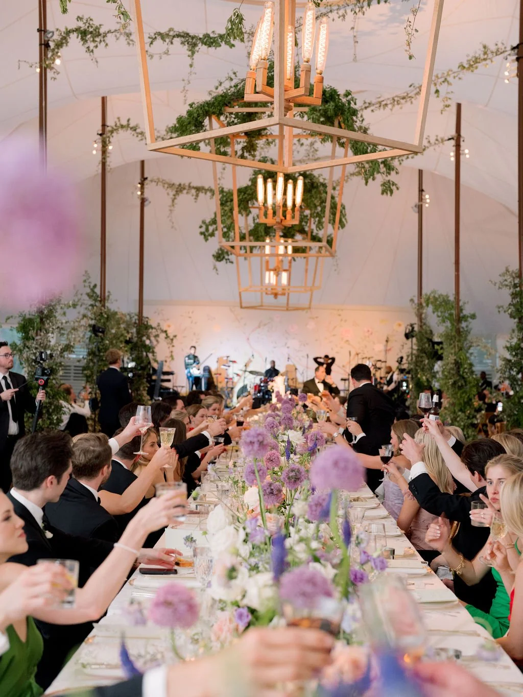 Guests raising glasses around a long floral-filled dinner table during an elegant tented destination wedding reception.