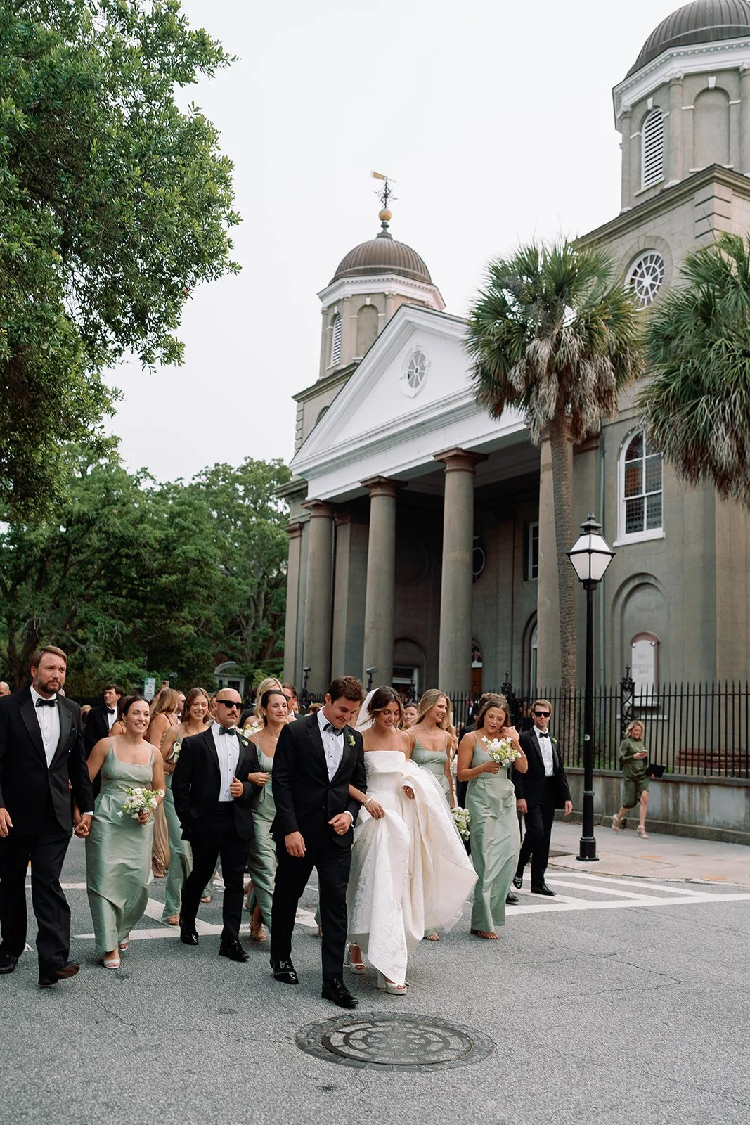 Bride, groom, and wedding party walking through downtown Charleston after a historic church ceremony.