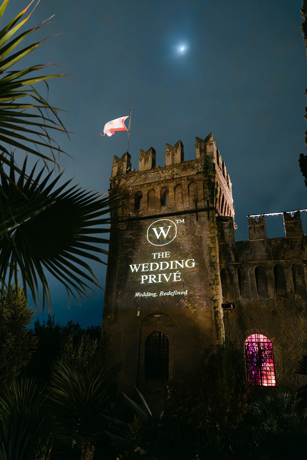 Historic Rome venue illuminated at night with The Wedding Privé logo projected across the stone façade beneath the moon.