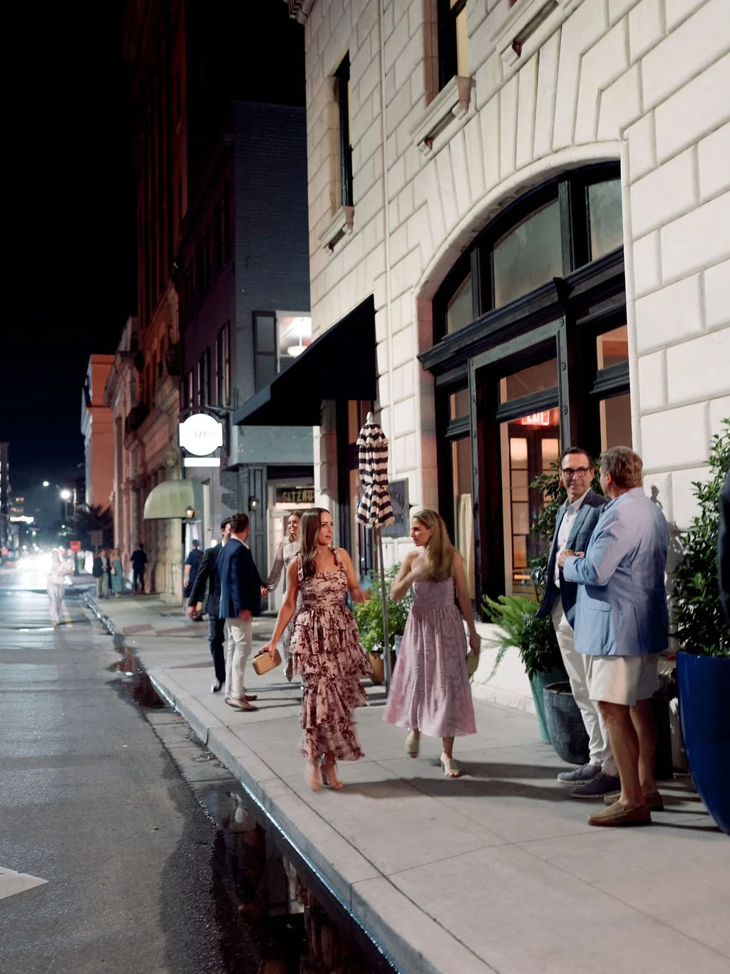 Wedding guests walking through a historic downtown district at night during a Southern destination wedding weekend.