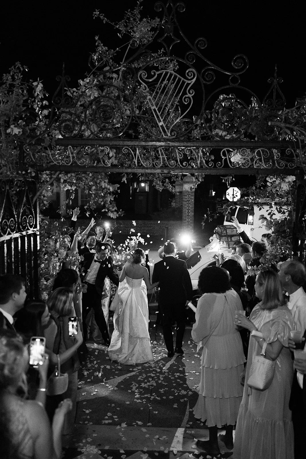 Black and white Charleston wedding sendoff with guests tossing petals as the couple exits toward a vintage getaway car.