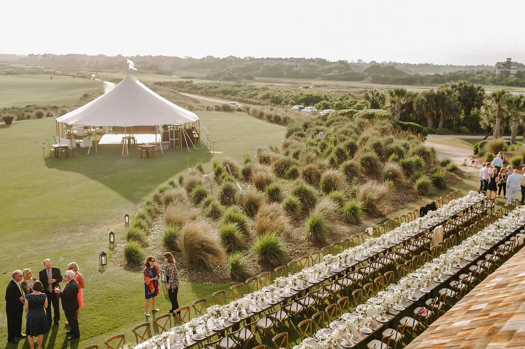 Long outdoor wedding dinner tables set beside a sailcloth tent on the lawn at The Ocean Course on Kiawah Island.