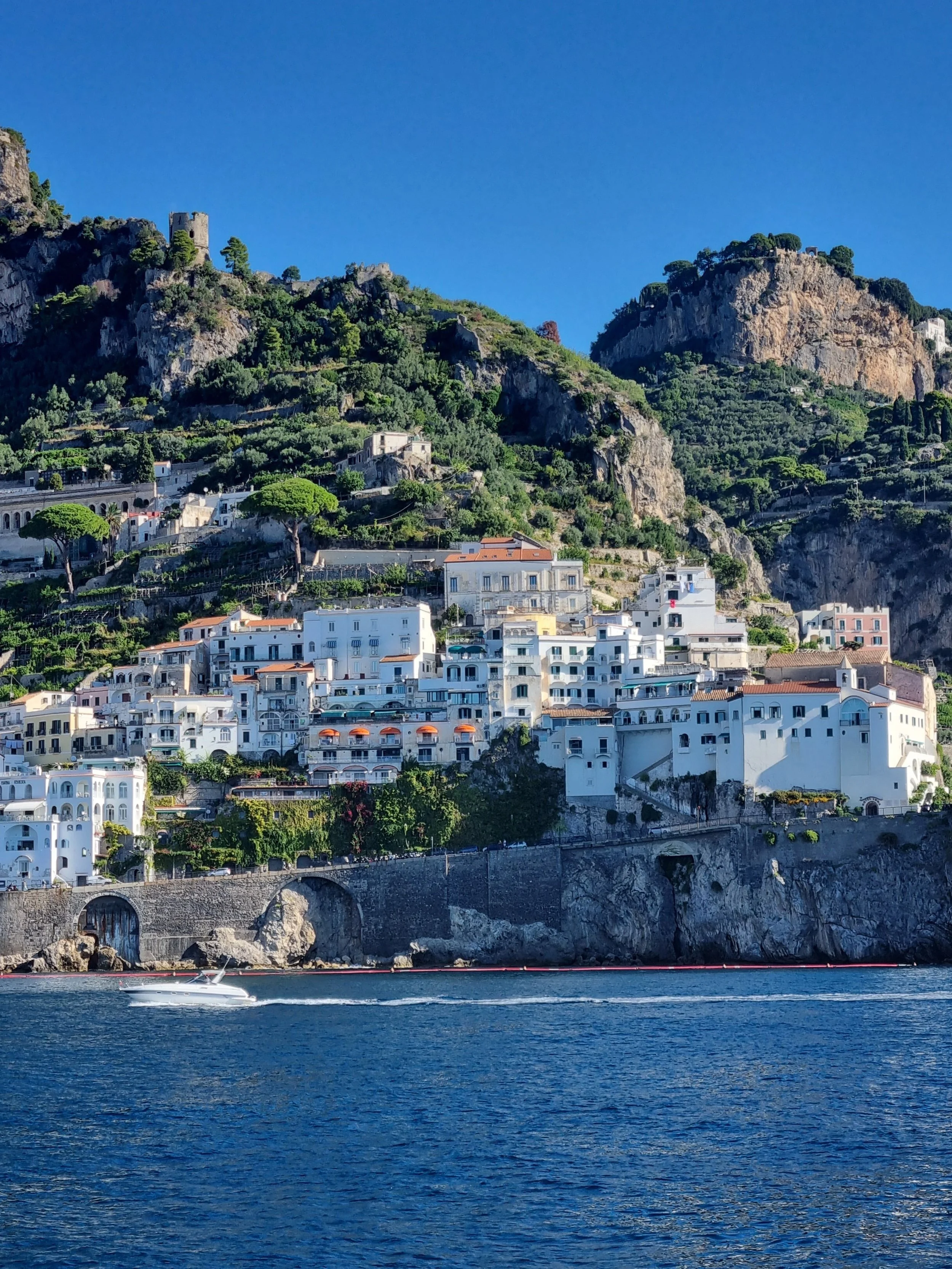 Cliffside buildings and lush hills rising above the blue Mediterranean Sea along Italy’s Amalfi Coast.