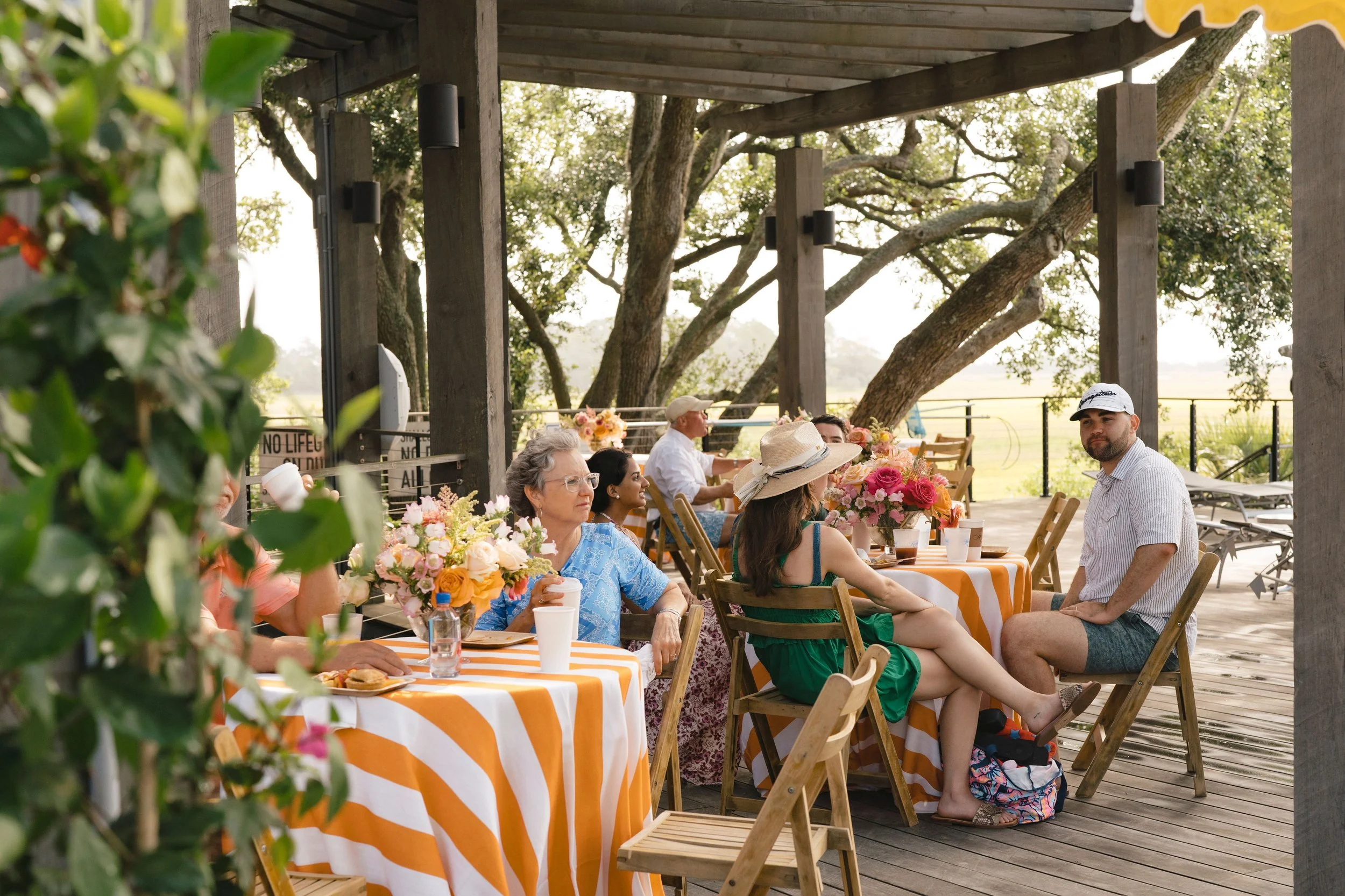 Wedding guests gathered for a relaxed morning-after brunch at orange striped tables on a shaded outdoor terrace.