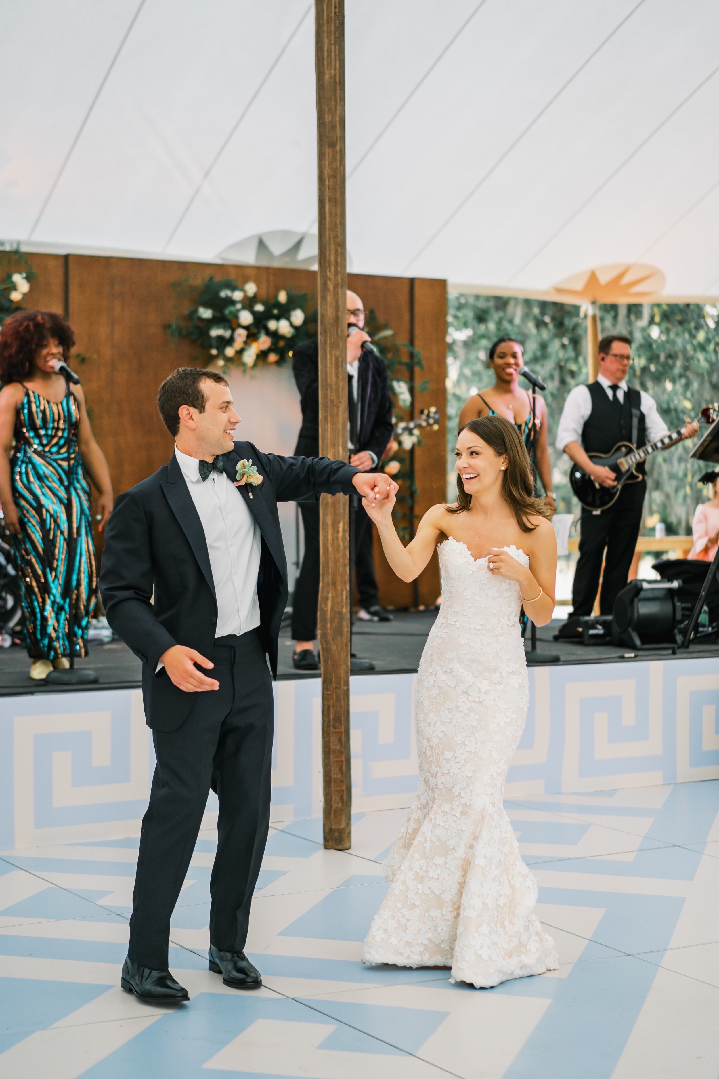 A newlywed couple sharing their first dance on a decorated dance floor, accompanied by a live band.
Brandon Lata Photography
Loluma
Charleston Wraps
Snyder Events
Juniper and Jasmine