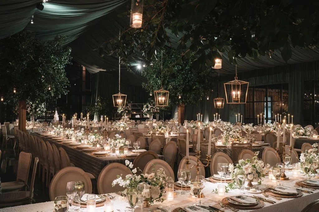 Evening wedding reception at The Dunlin with candlelit tables, hanging lanterns, layered florals, and dramatic green draping.