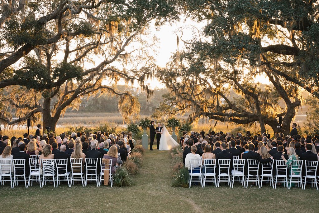 Wedding ceremony at The Dunlin framed by live oak trees and Spanish moss, with guests seated beside the marsh in the late-afternoon light.